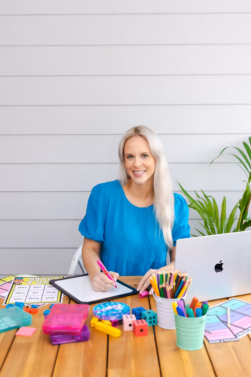 Tam sitting at a table with school supplies and her laptop. She is writing on a whiteboard.